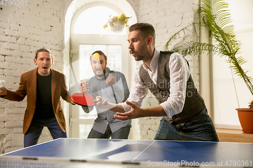 Image of Young people playing table tennis in workplace, having fun