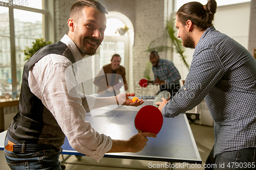 Image of Young people playing table tennis in workplace, having fun