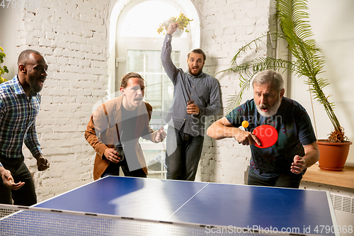 Image of Young people playing table tennis in workplace, having fun