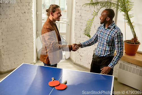 Image of Young men playing table tennis in workplace, having fun