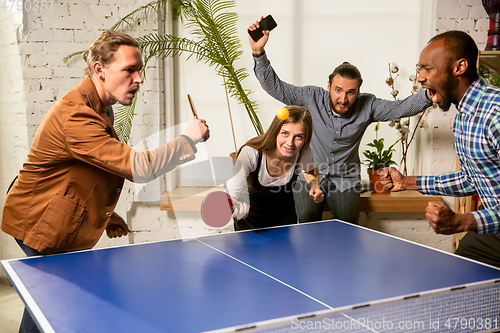 Image of Young people playing table tennis in workplace, having fun