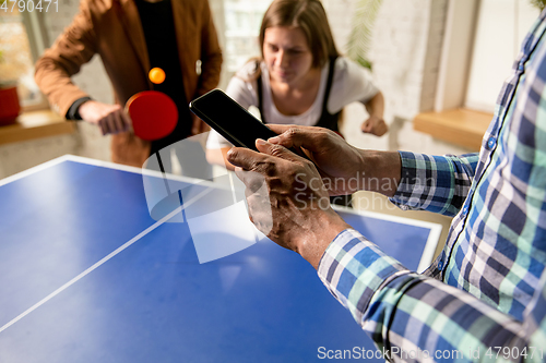 Image of Young people playing table tennis in workplace, having fun