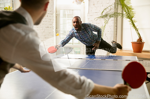 Image of Young men playing table tennis in workplace, having fun