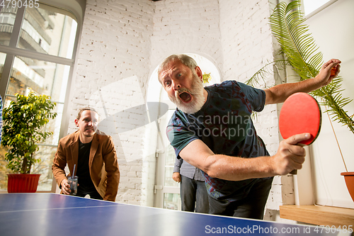 Image of Young people playing table tennis in workplace, having fun