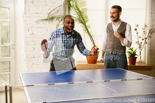 Image of Young men playing table tennis in workplace, having fun