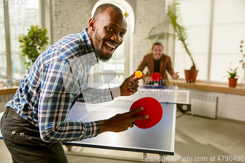 Image of Young men playing table tennis in workplace, having fun