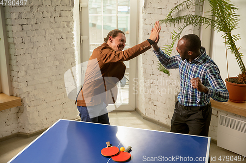 Image of Young men playing table tennis in workplace, having fun