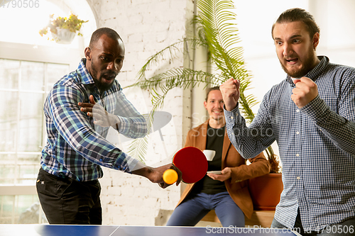 Image of Young people playing table tennis in workplace, having fun