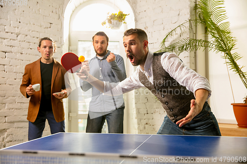 Image of Young people playing table tennis in workplace, having fun