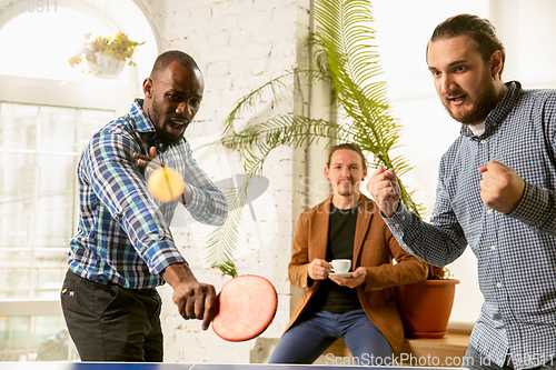 Image of Young people playing table tennis in workplace, having fun