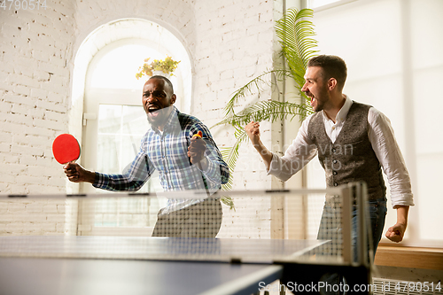 Image of Young men playing table tennis in workplace, having fun