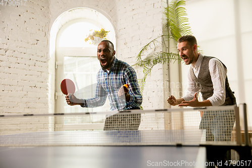 Image of Young men playing table tennis in workplace, having fun