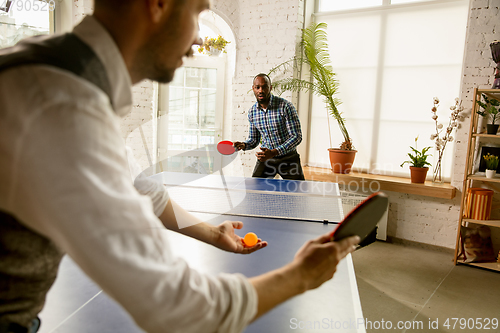 Image of Young men playing table tennis in workplace, having fun