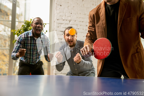 Image of Young people playing table tennis in workplace, having fun