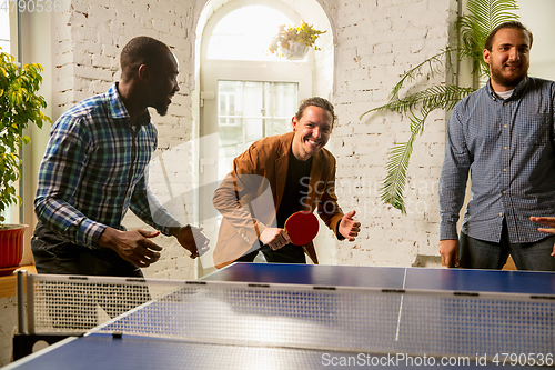 Image of Young people playing table tennis in workplace, having fun