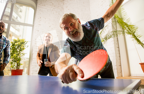 Image of Young people playing table tennis in workplace, having fun