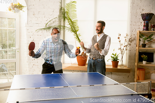 Image of Young men playing table tennis in workplace, having fun