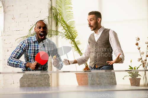 Image of Young men playing table tennis in workplace, having fun