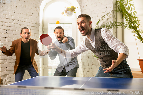 Image of Young people playing table tennis in workplace, having fun