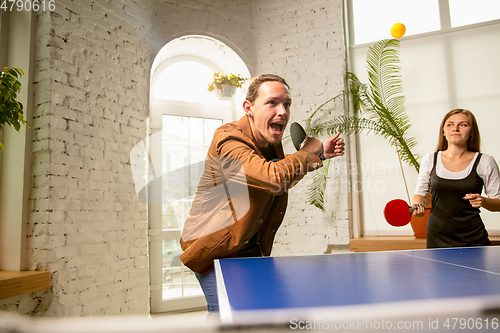 Image of Young people playing table tennis in workplace, having fun