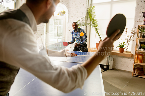 Image of Young men playing table tennis in workplace, having fun