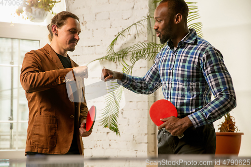 Image of Young men playing table tennis in workplace, having fun