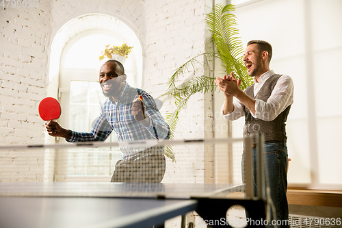 Image of Young men playing table tennis in workplace, having fun