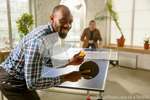 Image of Young men playing table tennis in workplace, having fun