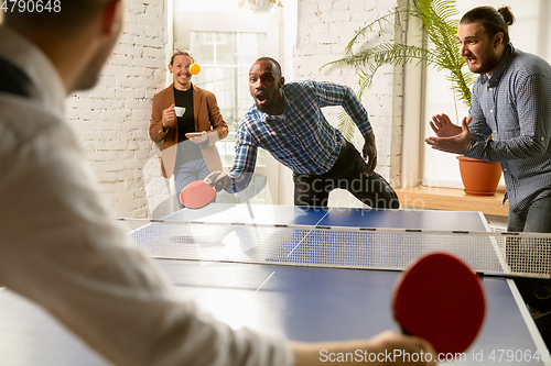 Image of Young people playing table tennis in workplace, having fun