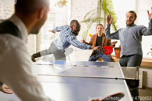 Image of Young people playing table tennis in workplace, having fun