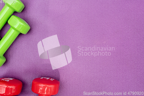 Image of Ladie's dumbbells over purple fitness mat, top view.
