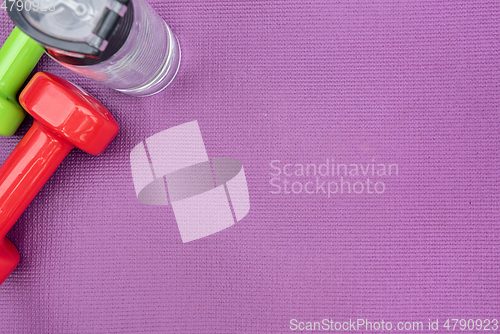 Image of Ladie's dumbbells and water bottle over purple fitness mat, top view.