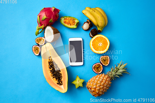 Image of exotic fruits around smartphone on blue background