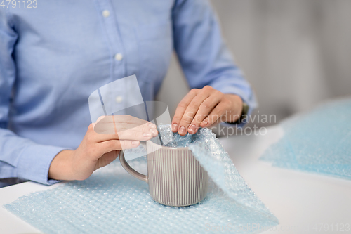 Image of woman packing mug to parcel box at post office