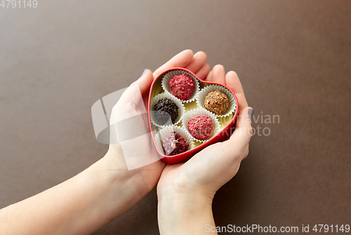 Image of hands with candies in heart shaped chocolate box