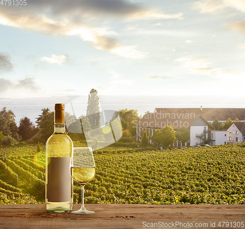 Image of Glass and bottle of wine on wooden rail with country rural scene in background