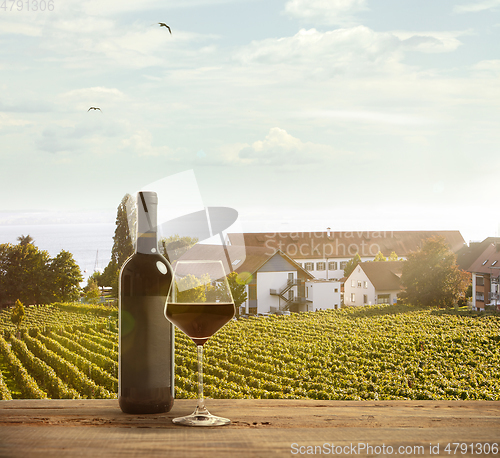 Image of Glass and bottle of wine on wooden rail with country rural scene in background