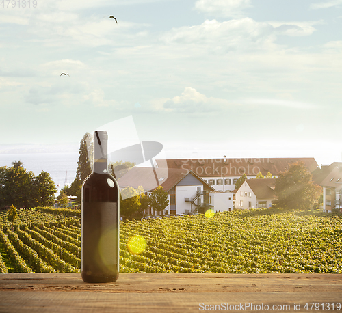 Image of Bottle of wine on wooden rail with country rural scene in background
