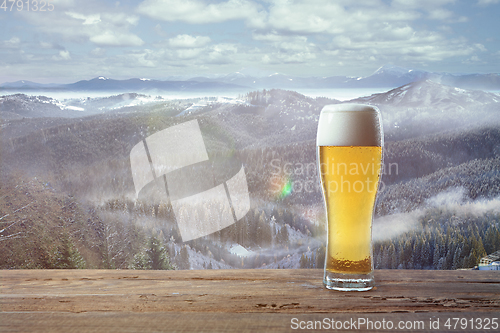 Image of Single light beer in glass and landscape of mountains on background