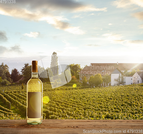 Image of Bottle of wine on wooden rail with country rural scene in background