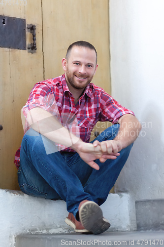 Image of young bearded man sitting at a door
