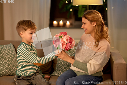 Image of smiling little son gives flowers to mother at home