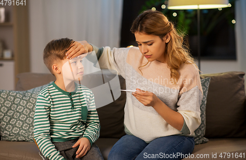 Image of sad mother with thermometer and ill son at home