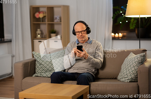 Image of senior man with smartphone and headphones at home