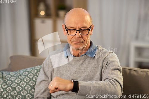 Image of senior man looking at wristwatch at home