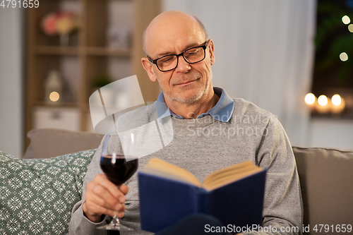 Image of happy senior man drinking wine and reading book