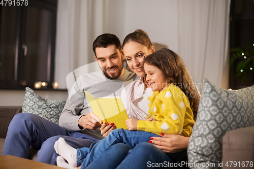 Image of happy family reading book at home at night