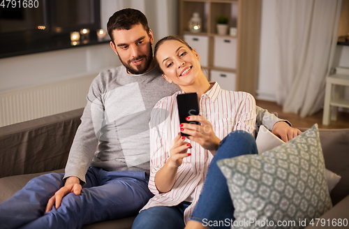 Image of happy couple with smartphone taking selfie at home