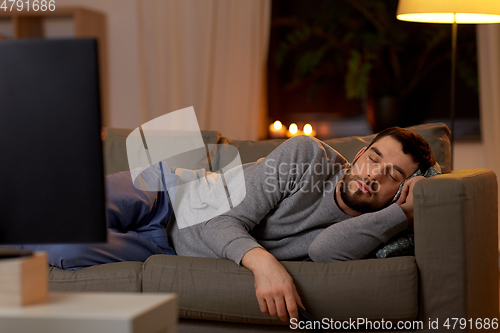 Image of man sleeping on sofa with tv remote at home