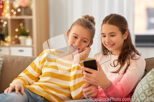 Image of happy girls with smartphone and earphones at home